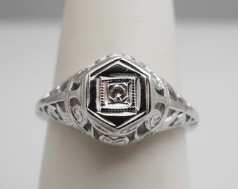 May include: A silver filigree ring with a small, clear diamond in the center.