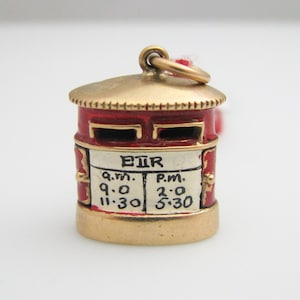 May include: Red enamel charm shaped like a British mailbox with gold accents. The mailbox has two slots and a sign that reads "EIR" and lists the hours of operation: "a.m. 9:00 11:30" and "p.m. 2:00 5:30".