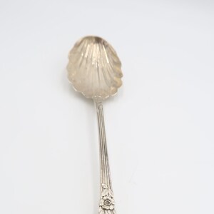 May include: A silver sugar spoon with a shell-shaped bowl and an ornate floral design on the handle.