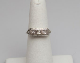 May include: A silver ring with three small square-shaped diamonds set in a decorative band.