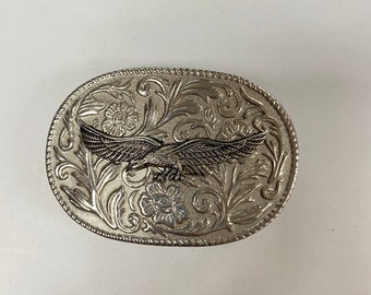 May include: Silver-toned belt buckle with an eagle design in the center. The buckle has an ornate floral pattern around the eagle.