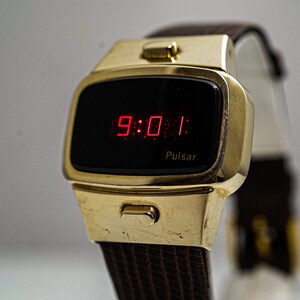 May include: A gold-toned Pulsar digital watch with a black face and red LED display showing the time 9:01. The watch has a brown leather strap.