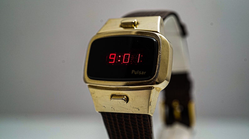 May include: A gold-toned Pulsar digital watch with a black face and red LED display showing the time 9:01. The watch has a brown leather strap.