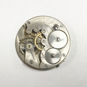 以下が含まれることがあります： 「LEHMANN WATCH CO. CHICAGO. ILL.」という刻印がされた銀製の懐中時計のムーブメントのクローズアップ