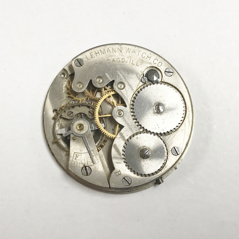 以下が含まれることがあります： 「LEHMANN WATCH CO. CHICAGO. ILL.」という刻印がされた銀製の懐中時計のムーブメントのクローズアップ