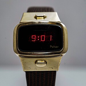 May include: A gold-toned Pulsar digital watch with a red LED display showing the time 9:01. The watch has a brown leather strap.