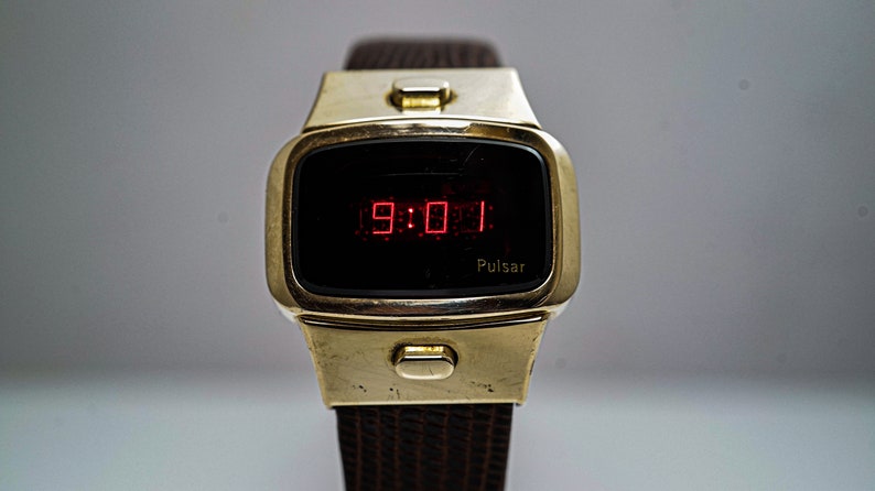 May include: A gold-toned Pulsar digital watch with a red LED display showing the time 9:01. The watch has a brown leather strap.