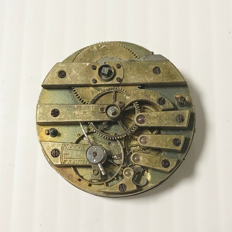 May include: Close-up of a vintage pocket watch movement with intricate gears and levers. The watch face is missing, revealing the inner workings of the timepiece.