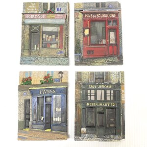 May include: Four decorative relief sculptures depicting French storefronts. The shops include a bookstore, a restaurant, a wine shop, and a shop with the text "France-Soir". Each has architectural details and is painted in muted tones.