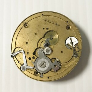 May include: A detailed view of a vintage watch movement. The circular brass plate houses numerous small gears, levers, and a balance wheel. The number "188945" is stamped on the brass. The mechanism is a complex arrangement of tiny components.