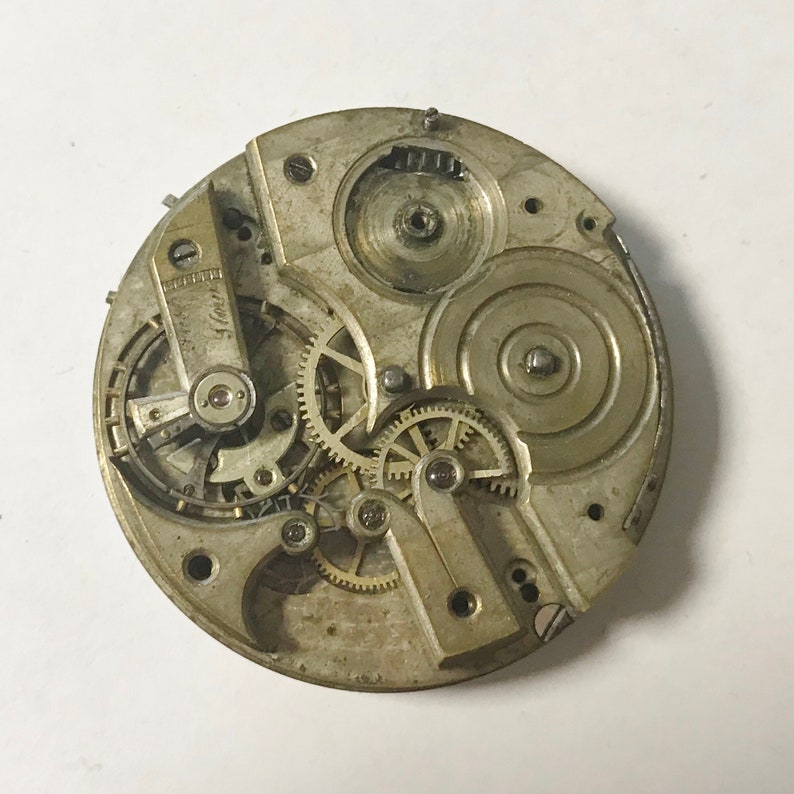 May include: Close-up of a silver pocket watch movement with intricate gears and a winding mechanism. The watch face is not visible.