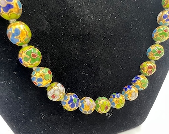 May include: A necklace made of round, colorful beads with gold accents. The beads are decorated with a floral pattern in shades of blue, green, yellow, and white.