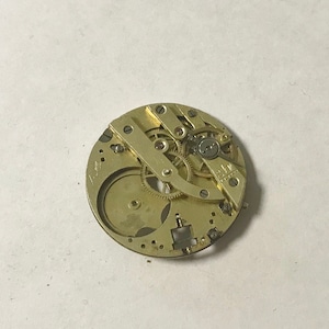 May include: A close-up of a gold-colored watch movement with intricate gears and a small metal plate with the text "E.L.F. Swiss Made" visible.
