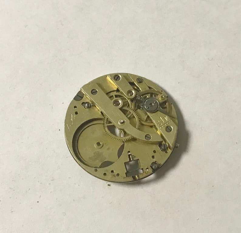May include: A close-up of a gold-colored watch movement with intricate gears and a small metal plate with the text "E.L.F. Swiss Made" visible.