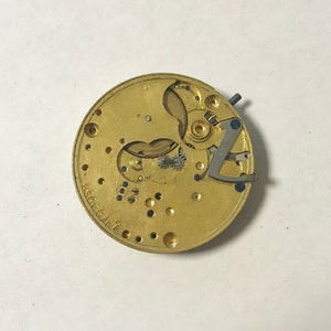 May include: A gold-colored watch movement with intricate gears and a silver-colored lever. The movement is labeled "2361 6142".