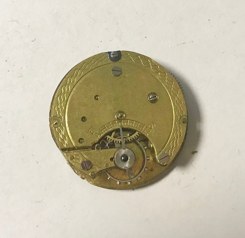 May include: A gold-colored pocket watch movement with visible gears and a decorative pattern on the back.