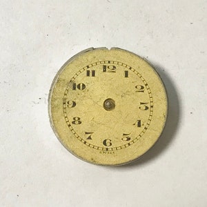 Puede incluir: Una esfera de reloj redonda de color crema con marcadores de hora en n&uacute;meros romanos negros y marcadores de minutos en n&uacute;meros ar&aacute;bigos negros. La esfera est&aacute; rodeada por un borde de metal plateado con la palabra "Swiss" impresa en la parte inferior.
