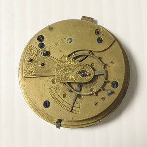 Op de afbeelding: Close-up van een goudkleurig zakhorloge-uurwerk met ingewikkelde gravures en het zichtbare nummer "504756". De wijzerplaat van het horloge ontbreekt.