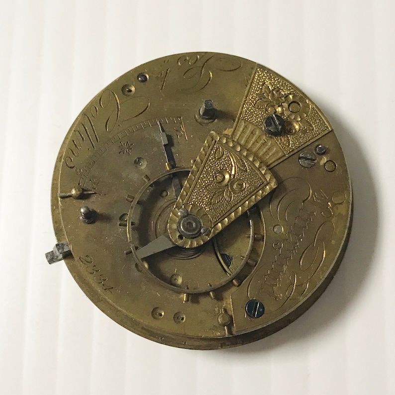 Pu&ograve; includere: Un orologio da tasca in oro con incisioni intricate e un meccanismo di orologeria dettagliato. Il quadrante dell'orologio presenta un design floreale decorativo e l'iscrizione "23kt".