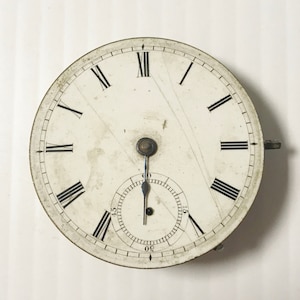 May include: A white pocket watch with Roman numeral hour markers and a black second hand. The watch face is slightly aged and has a few scratches.