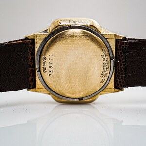 May include: A gold-tone Pulsar watch with a brown leather strap. The back of the watch has the text "Pulsar", "729771", and "ONE COMPUTER INC.  THE COLLECTIBLES  USA". The strap is labelled "Lizard"