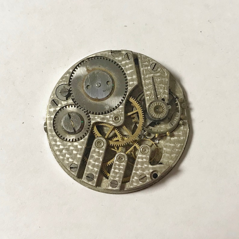 May include: A silver watch movement with exposed gears and a patterned back plate.