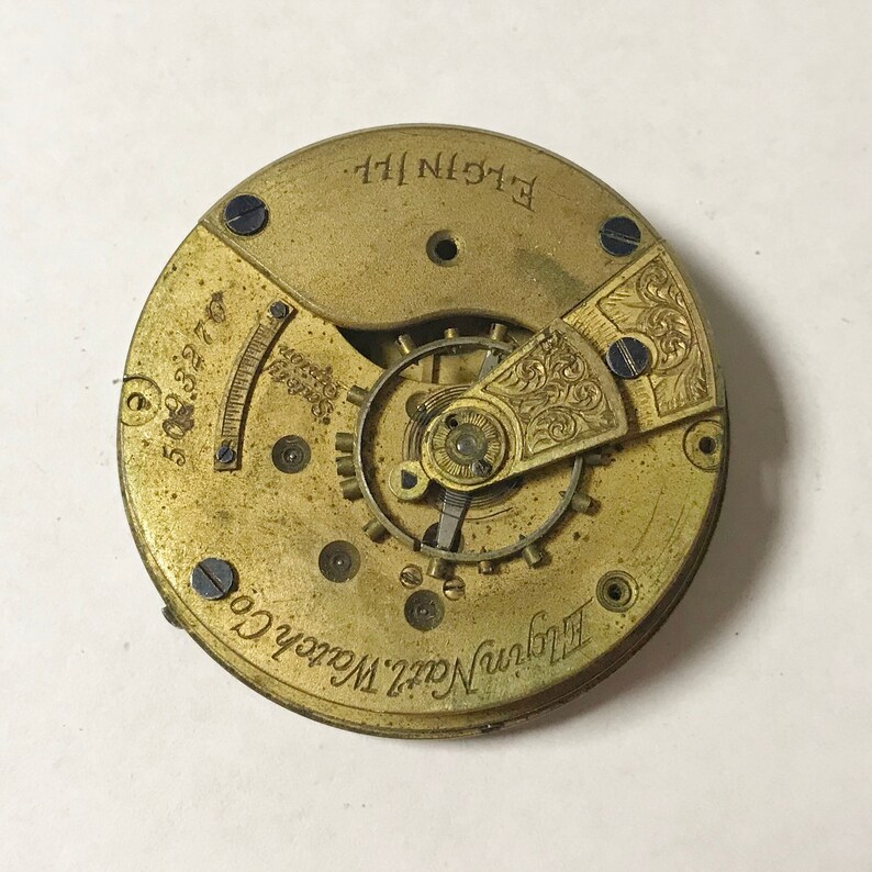 May include: Close-up of the inner workings of a gold-toned pocket watch with the text "Elgin Natl. Watch Co." and "ELGIN, ILL." on the face.