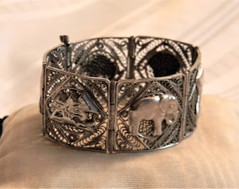 Op de afbeelding: Een zilveren armband met een filigraanontwerp en dierlijke motieven. De armband is gemaakt van delicaat draadwerk en heeft een olifant, een vogel en andere dieren.