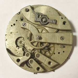 Pu&ograve; includere: Una vista ravvicinata di un movimento di orologio da tasca argentato con ingranaggi e leve intricate. L'orologio &egrave; smontato e disposto su una superficie bianca.