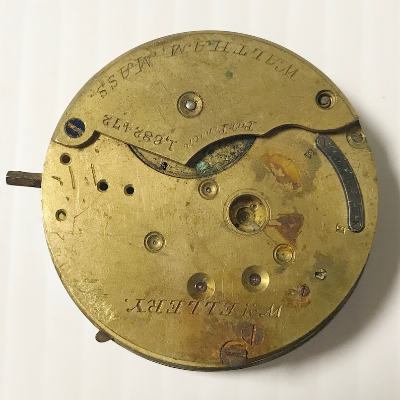 May include: A vintage brass watch movement with the text "WALTHAM, MASS" and "W. ELLERY" engraved on the surface. The movement also features the serial number "1.682.473". The watch mechanism has various gears, screws, and other components.