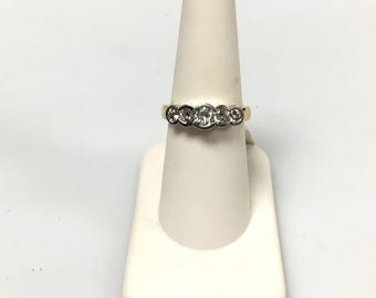May include: A gold and silver ring with five clear gemstones. The ring is displayed on a white ring holder against a white background. The gemstones are round and set in a silver band.