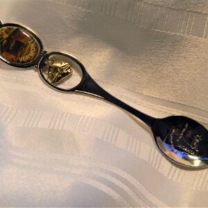 May include: A silver souvenir spoon with a gold-colored charm and a round image of a building with the word "Vermont" on it.