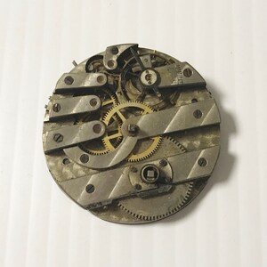 May include: Close-up of a silver and gold pocket watch movement with intricate gears and levers.