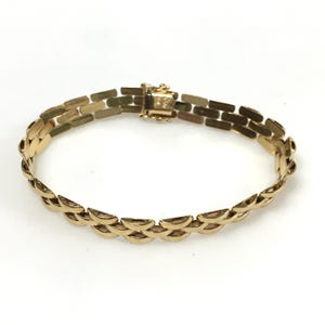 May include: A gold-colored bracelet with a rectangular and half-moon link design. The bracelet has a clasp closure and is displayed on a white background. The jewelry piece is a classic accessory.