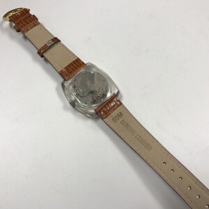 Peut inclure: Un bracelet de montre en cuir marron avec un cadran de montre transparent et le texte "20M GENUINE LEATHER" imprim&eacute; sur le bracelet.