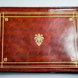 May include: A brown leather-bound journal with a gold embossed fleur-de-lis design and a gold border.