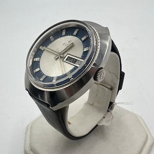 May include: A silver-toned wristwatch with a black leather band. The watch face is white with black markings and a blue outer ring. The date window displays "SAT 20". The watch brand is "ELG".