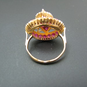 May include: A gold ring with a round, red gemstone surrounded by smaller red gemstones. The ring has a delicate, intricate design.