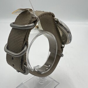 May include: A silver wristwatch with a brown canvas watch band. The watch is on a display stand.