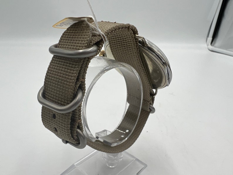 May include: A silver wristwatch with a brown canvas watch band. The watch is on a display stand.