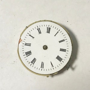 May include: White clock face with black Roman numeral hour markers and black minute markers. The clock face is surrounded by a gold-coloured metal rim.
