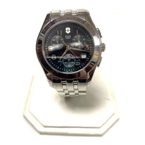 May include: A silver-toned Swiss Army chronograph watch with a black dial. The watch features a date display, multiple sub-dials, and a stainless steel band. The watch is displayed on a white surface.