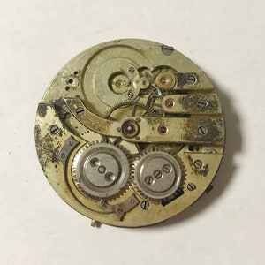K&ouml;nnte beinhalten: Nahaufnahme eines silbernen Taschenuhrwerks mit komplizierten Zahnr&auml;dern und Hebeln. Das Zifferblatt der Uhr fehlt, wodurch das Innenleben des Zeitmessers sichtbar wird.