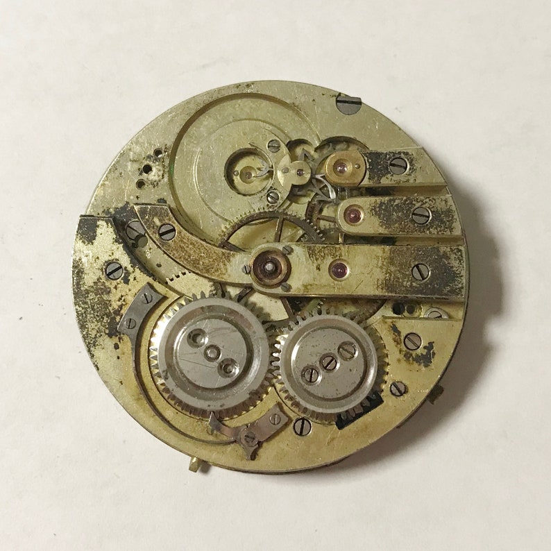 K&ouml;nnte beinhalten: Nahaufnahme eines silbernen Taschenuhrwerks mit komplizierten Zahnr&auml;dern und Hebeln. Das Zifferblatt der Uhr fehlt, wodurch das Innenleben des Zeitmessers sichtbar wird.