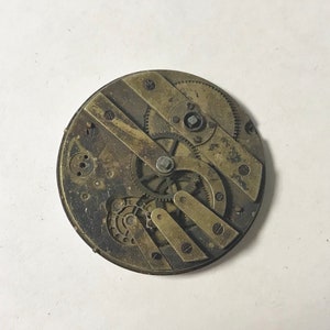 Puede incluir: Primer plano de un movimiento de reloj de bolsillo vintage con engranajes intrincados y componentes de lat&oacute;n.