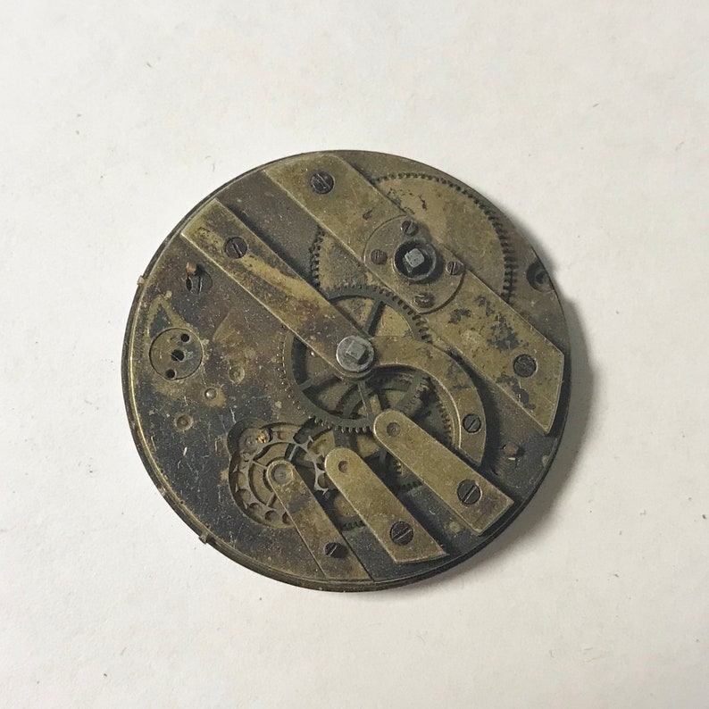 Puede incluir: Primer plano de un movimiento de reloj de bolsillo vintage con engranajes intrincados y componentes de lat&oacute;n.