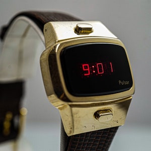 May include: A gold-toned Pulsar digital watch with a black face and red LED display showing the time 9:01. The watch has a brown leather strap.