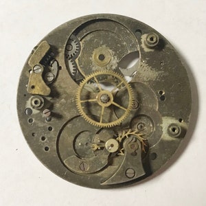 Pu&ograve; includere: Primo piano di un movimento di orologio argentato con pi&ugrave; ingranaggi e un ingranaggio dorato al centro.
