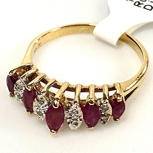 May include: A gold ring featuring alternating marquise-cut rubies and small round diamonds. The ring has a classic design with a polished gold band and is set with seven gemstones.