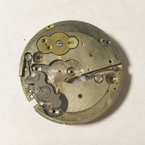 Op de afbeelding: Close-up van een zilveren uurwerk met tandwielen en een goudkleurig opwindmechanisme.